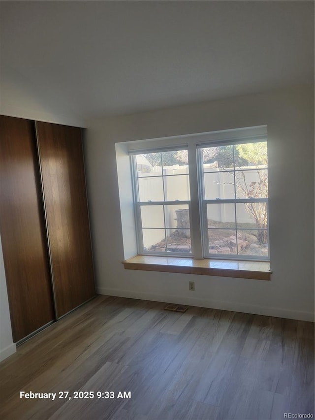 unfurnished bedroom featuring a closet, wood finished floors, visible vents, and baseboards