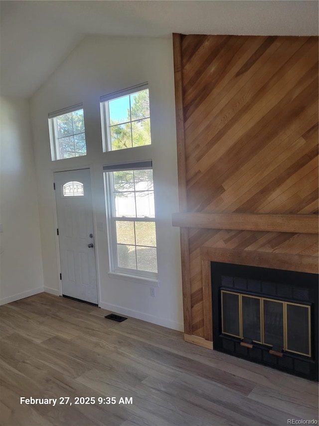 foyer featuring visible vents, a glass covered fireplace, wood finished floors, high vaulted ceiling, and baseboards