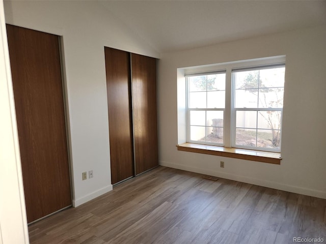 unfurnished bedroom featuring visible vents, baseboards, wood finished floors, vaulted ceiling, and a closet