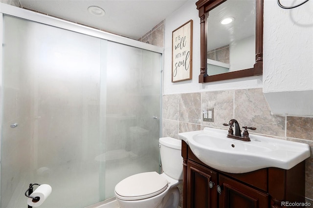 bathroom featuring vanity, toilet, tile walls, and a shower with shower door