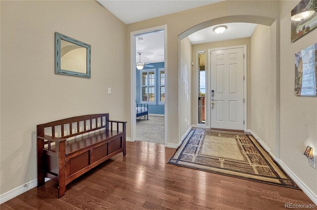 foyer entrance with arched walkways, baseboards, and wood finished floors