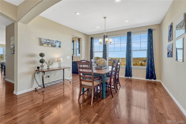 dining area featuring arched walkways, an inviting chandelier, wood finished floors, and baseboards