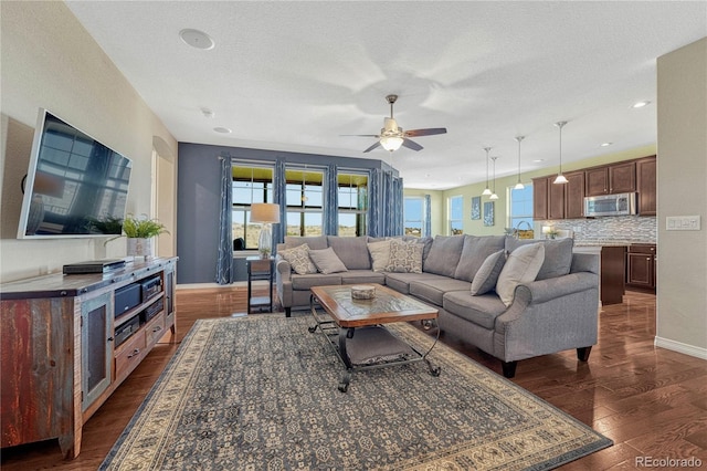 living room featuring a ceiling fan, a textured ceiling, baseboards, and dark wood-style flooring