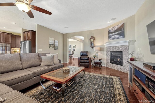 living room with arched walkways, a textured ceiling, dark wood-style flooring, baseboards, and a tiled fireplace