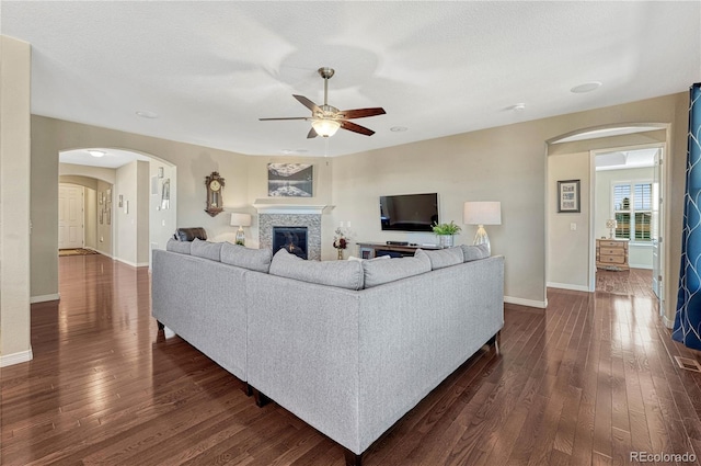 living room with dark wood-style floors, arched walkways, a ceiling fan, a textured ceiling, and baseboards