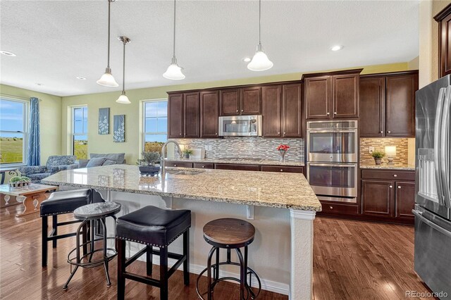 kitchen with a breakfast bar, stainless steel appliances, dark wood-type flooring, open floor plan, and a sink