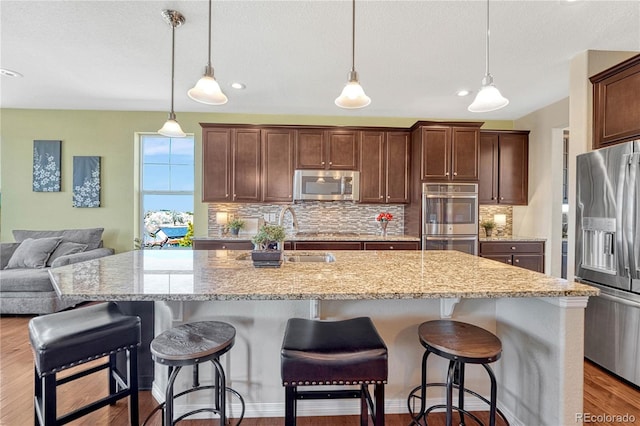 kitchen with wood finished floors, appliances with stainless steel finishes, backsplash, and light stone counters