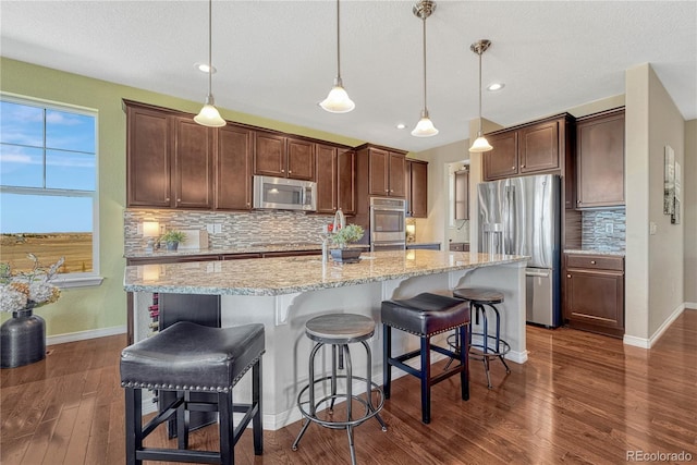 kitchen featuring light stone counters, stainless steel appliances, a kitchen breakfast bar, dark wood finished floors, and a center island with sink