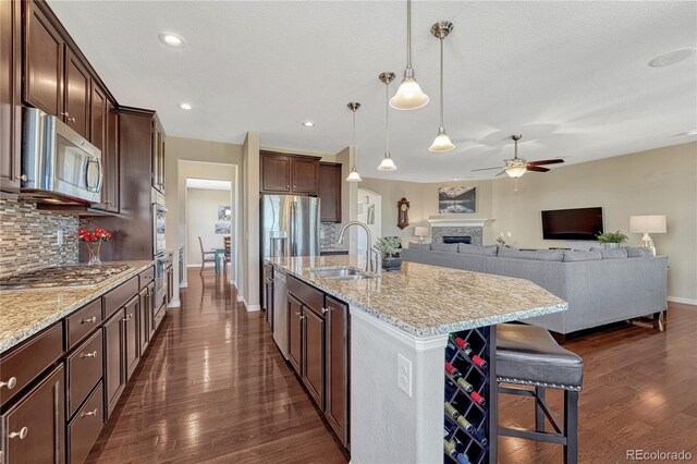 kitchen featuring light stone counters, backsplash, appliances with stainless steel finishes, a sink, and a kitchen breakfast bar