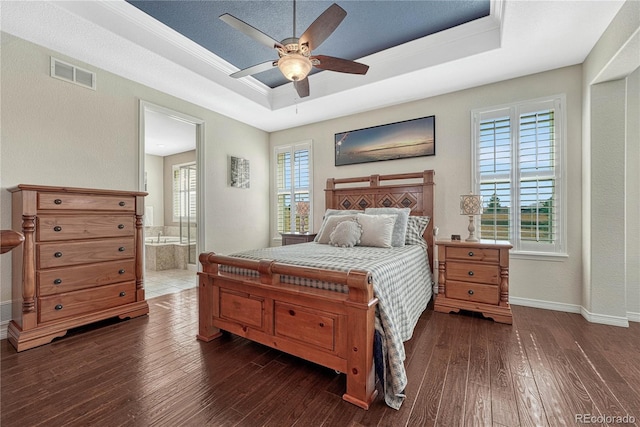 bedroom featuring dark wood-style floors, a tray ceiling, visible vents, and multiple windows