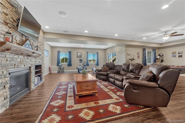 living room featuring a textured ceiling, baseboards, wood finished floors, and a stone fireplace