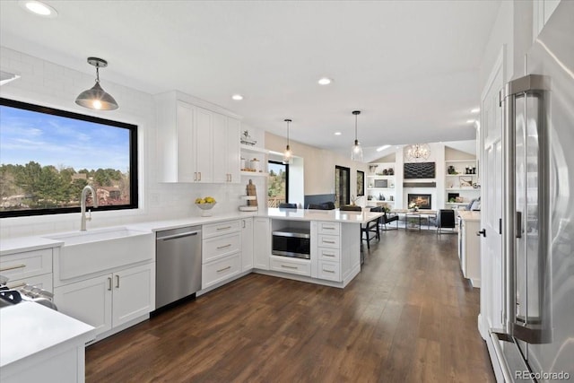 kitchen with a peninsula, dark wood-style floors, light countertops, a sink, and appliances with stainless steel finishes