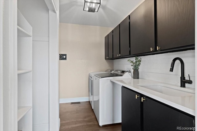 laundry room featuring cabinet space, dark wood-style flooring, washing machine and clothes dryer, a sink, and baseboards
