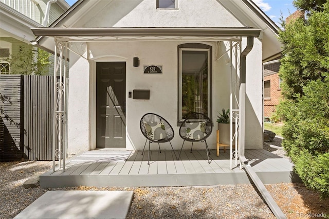 view of exterior entry with fence and stucco siding