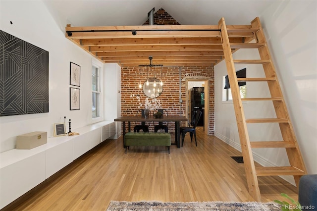 dining space featuring visible vents, brick wall, vaulted ceiling, light wood-style floors, and a chandelier