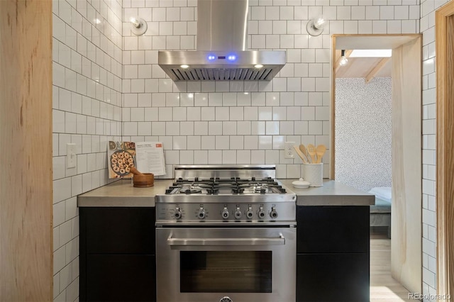 kitchen featuring range hood, tasteful backsplash, light countertops, dark cabinets, and high end stove