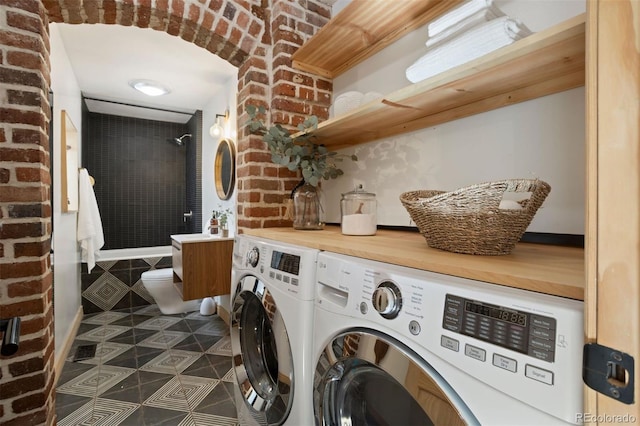 washroom with laundry area, brick wall, dark tile patterned floors, and washing machine and clothes dryer