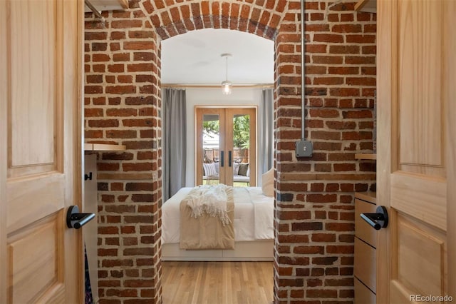 unfurnished bedroom with light wood finished floors, brick wall, and french doors