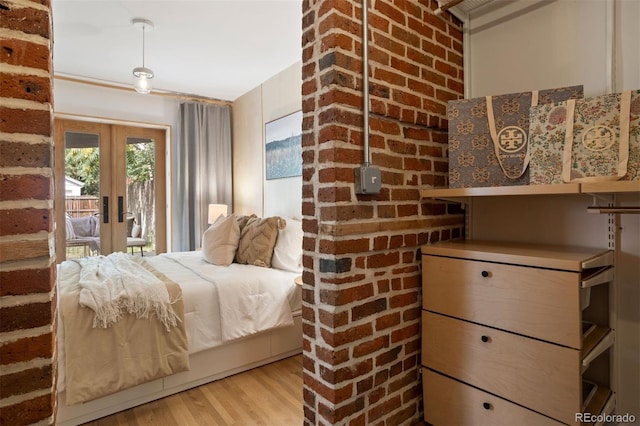 bedroom with access to outside, french doors, brick wall, and wood finished floors