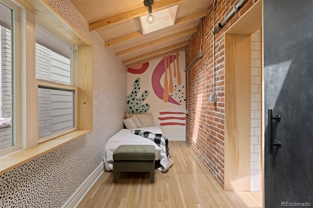 sitting room with beam ceiling, a barn door, brick wall, wood finished floors, and baseboards