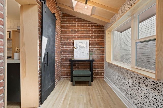 unfurnished room featuring lofted ceiling with beams, a barn door, brick wall, wood finished floors, and baseboards