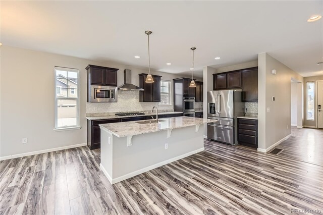 kitchen with a sink, stainless steel appliances, wall chimney exhaust hood, and a healthy amount of sunlight