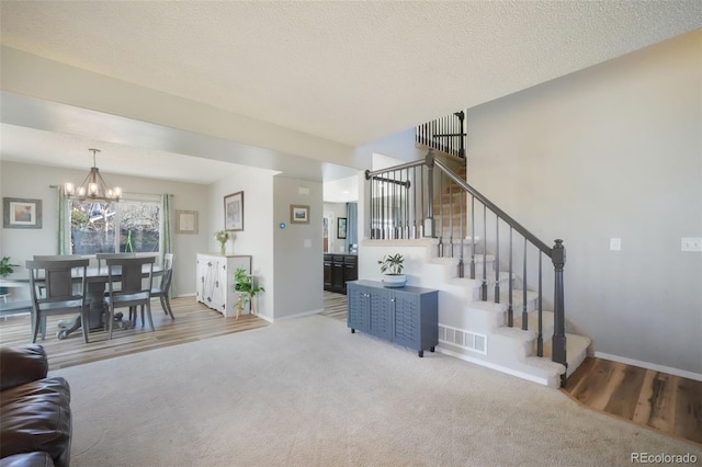 carpeted living area with visible vents, a notable chandelier, a textured ceiling, stairway, and baseboards