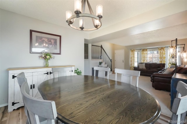 dining room featuring stairway, a textured ceiling, an inviting chandelier, and light wood finished floors