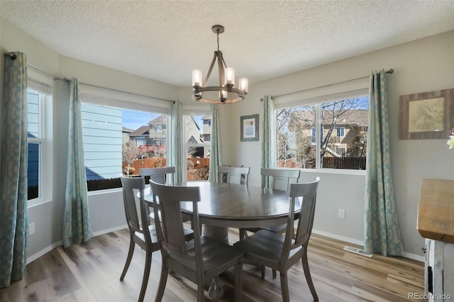 dining area with an inviting chandelier, baseboards, light wood-type flooring, and a textured ceiling