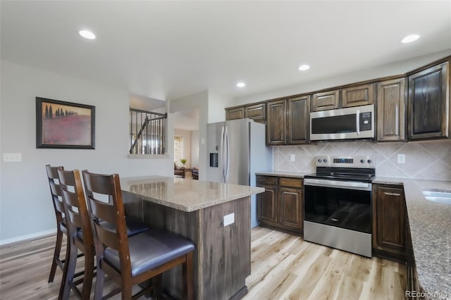 kitchen featuring light stone counters, stainless steel appliances, light wood-style flooring, and decorative backsplash