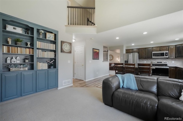 living area with baseboards, visible vents, a high ceiling, recessed lighting, and light carpet