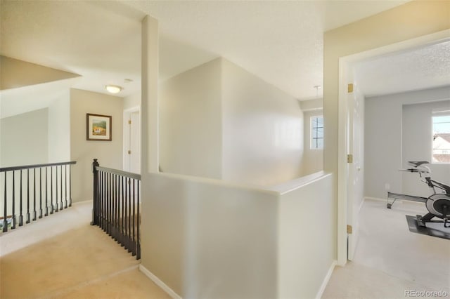 corridor featuring an upstairs landing, carpet flooring, a textured ceiling, and baseboards