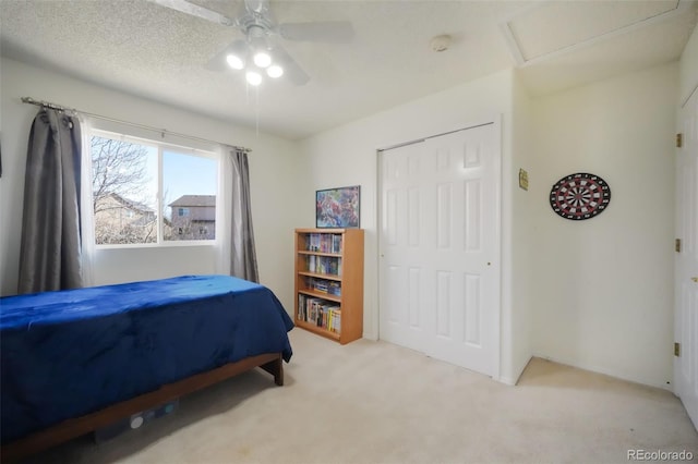 bedroom featuring ceiling fan, attic access, light carpet, a closet, and a textured ceiling