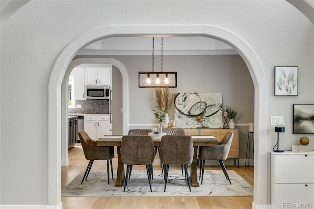 1311 Fletcher Dr, Erie, CO 80516 - dining room with light wood finished floors, crown molding, arched walkways, a chandelier, and baseboards