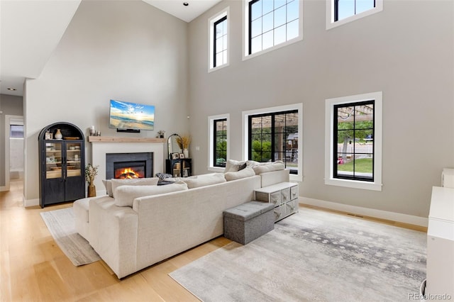 1311 Fletcher Dr, Erie, CO 80516 - living room featuring light wood finished floors, a high ceiling, a glass covered fireplace, and baseboards