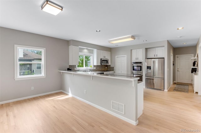 1311 Fletcher Dr, Erie, CO 80516 - kitchen with stainless steel appliances, a peninsula, white cabinetry, light wood-style flooring, and a kitchen bar