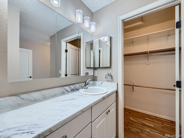 bathroom featuring a textured ceiling, wood finished floors, a walk in closet, vanity, and baseboards