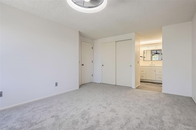 unfurnished bedroom featuring light carpet, a sink, a textured ceiling, connected bathroom, and a closet