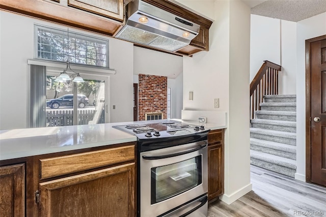 kitchen featuring stainless steel electric range oven, under cabinet range hood, light wood-style floors, baseboards, and light countertops