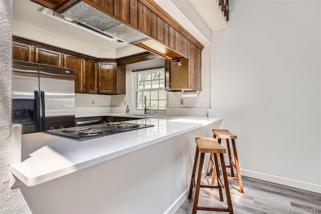 kitchen with stainless steel refrigerator with ice dispenser, a sink, cooktop, wood finished floors, and light countertops
