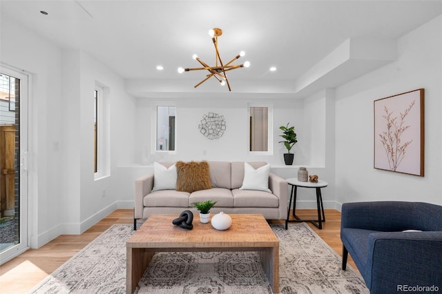 living area featuring a chandelier, light wood-type flooring, baseboards, recessed lighting, and a tray ceiling