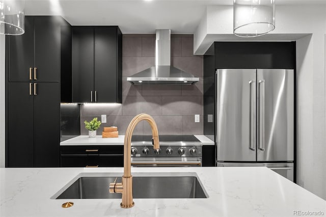 kitchen with premium appliances, wall chimney exhaust hood, dark cabinetry, and a sink