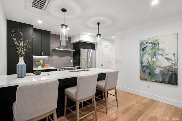 kitchen with dark cabinets, a sink, light wood finished floors, backsplash, and pendant lighting