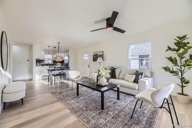living area with baseboards, a ceiling fan, and light wood-style flooring
