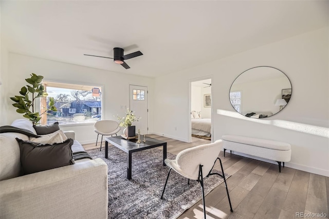 living room featuring baseboards, a ceiling fan, and light wood-style flooring
