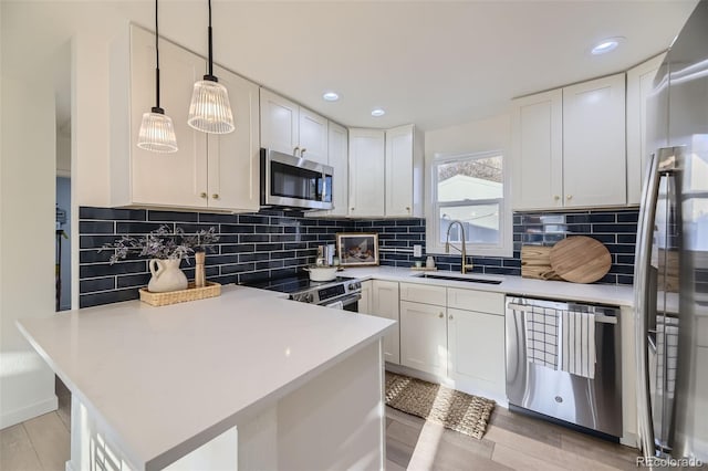 kitchen with a sink, a peninsula, white cabinets, and stainless steel appliances