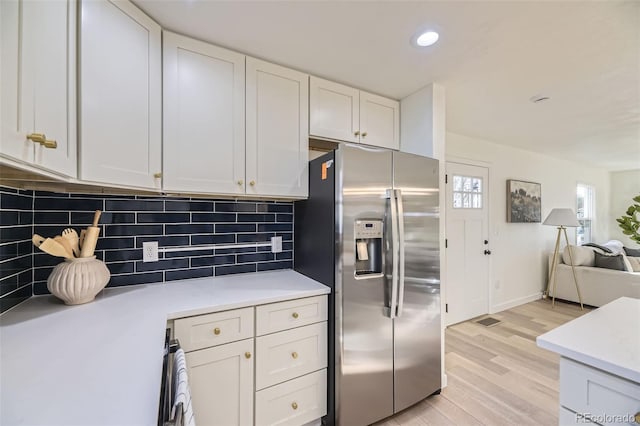 kitchen featuring decorative backsplash, open floor plan, stainless steel fridge, light countertops, and light wood-type flooring