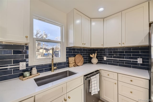 kitchen with stainless steel dishwasher, decorative backsplash, light countertops, white cabinetry, and a sink
