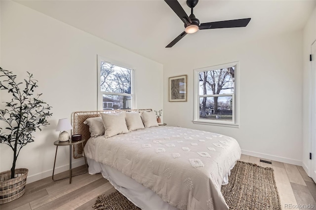 bedroom featuring baseboards, a ceiling fan, light wood finished floors, and multiple windows