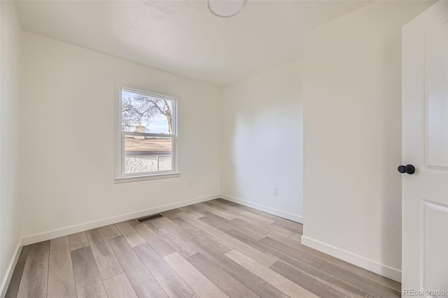 empty room featuring light wood-style floors, baseboards, and visible vents